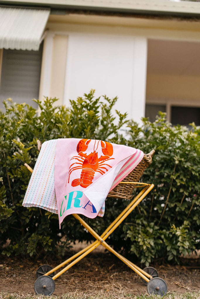 Pink towel with a lobster design on a wooden cart outdoors.