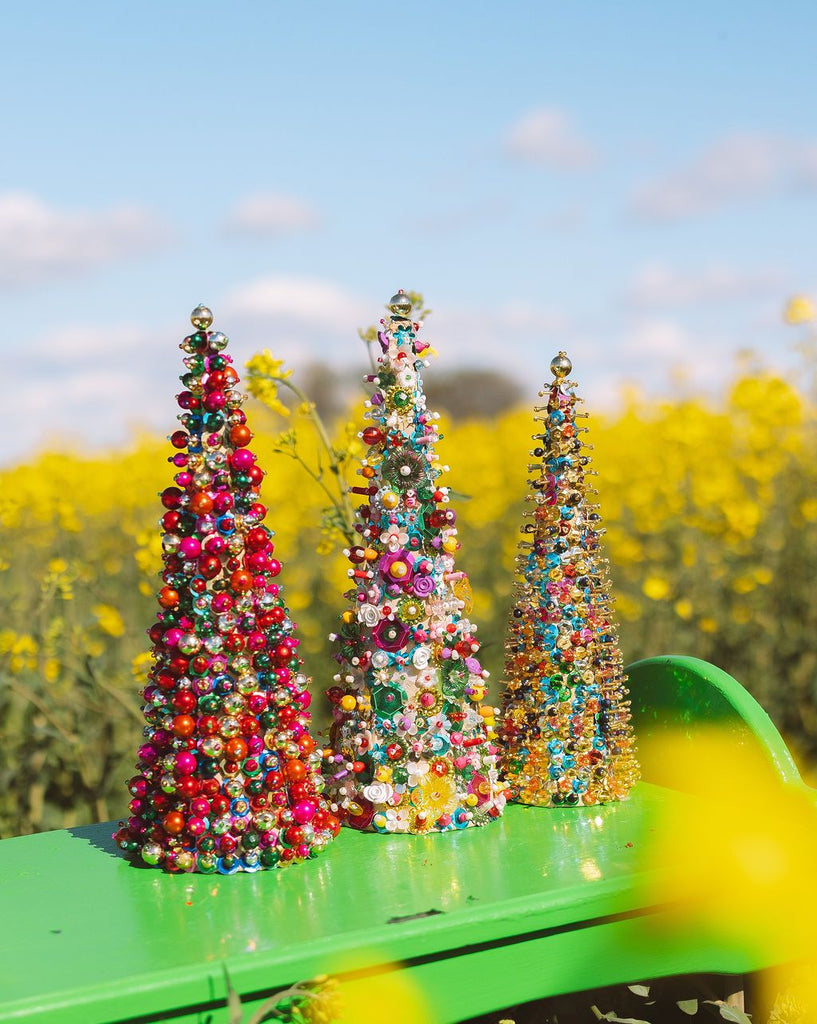 Colorful beaded trees on a green surface with a yellow field and blue sky in the background